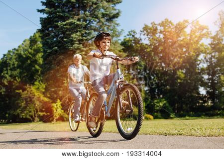 Increasing speed. Inventive easy going nice kid and his grandparent having fun while spending his day with his grandpa and riding bikes with him