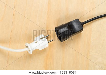 Disconnected white european power cable plug with black connector cable on wooden floor or table background