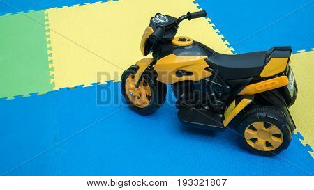 Close Up Of Yellow Motocycle Toy On Rubber Floor With Copy Space At Playground. Cute Little Motocycl