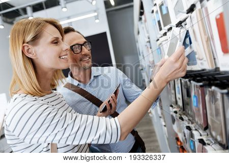  Side view on positive customers standing at a store display and shopping for phone cases while walking around the department store.
