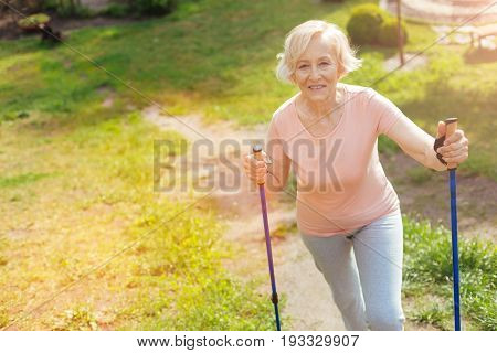 Positive mood. Delighted positive elderly woman smiling eng enjoying her walk while being in the forest