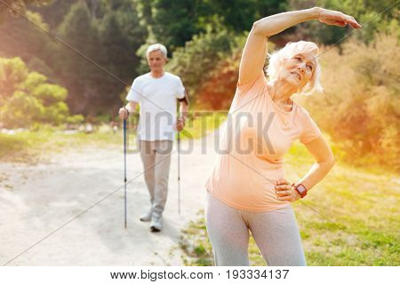 Staying fit. Pleasant active senior woman standing on the grass and doing physical exercises while staying fit