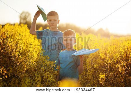 Two little boys friends with blue paper planes in summer yellow field. Brother love. Concept friendship