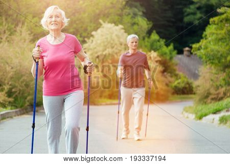 Outdoor training. Positive active nice couple holding walking poles and practicing sports activities while having an outdoor training