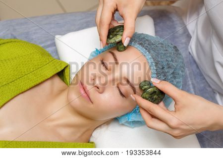 Spa treatment. Facial massage with jade stones. Alternative medicine. Massage of forehead zone. Guasha
