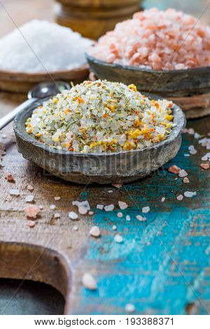 Different types of natural salt in stone bowls on wooden surface. White sea salt pink Himalayan salt Spiced salt with rosemary