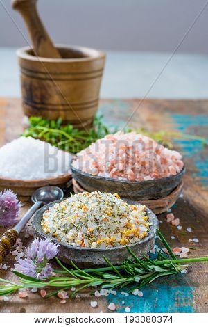 Different types of natural salt in stone bowls on wooden surface. White sea salt pink Himalayan salt Spiced salt with rosemary