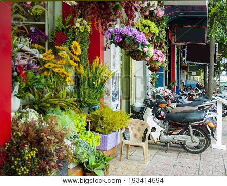 Street in a Vietnamese city next to a flower shop and a lot of parked bikes.