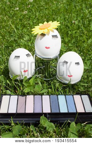 three eggs with make-up on a metal stand on green grass in front of the kit eyeshadow
