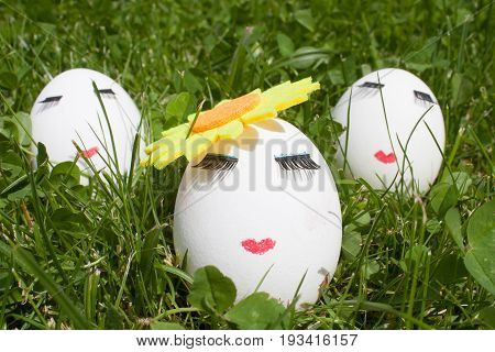 three eggs with make-up on green grass, one in the foreground