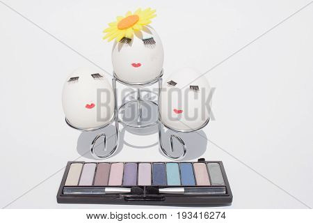 three eggs with make up on a metal stand in front of the kit eyeshadow on white background