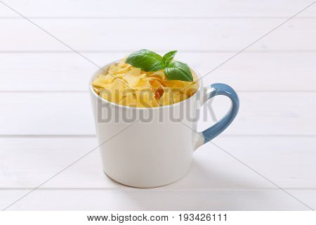 mug of quadretti - square shaped pasta on white wooden background