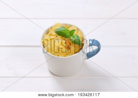 mug of quadretti - square shaped pasta on white wooden background