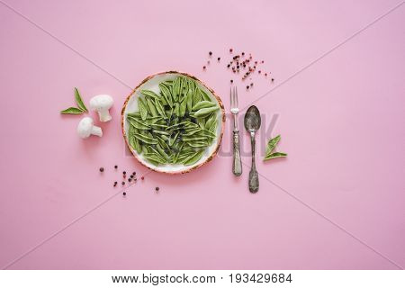 Dry green foglie pasta made from durum wheat semolina dried tomatoes spinach and water. Top view on vintage plate and old silver cutlery with Champignons and pepper on pink background