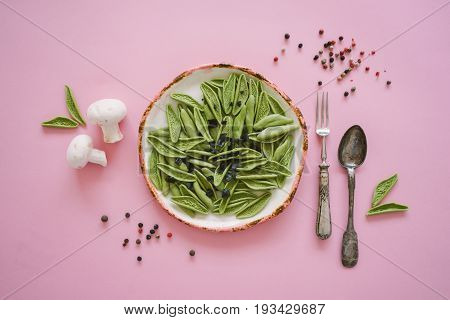 Dry green foglie pasta made from durum wheat semolina dried tomatoes spinach and water. Top view on vintage plate and old silver cutlery with champignons and pepper on pink background