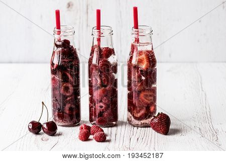 Detox Water In Three Bottles With Berries On White Wooden Background