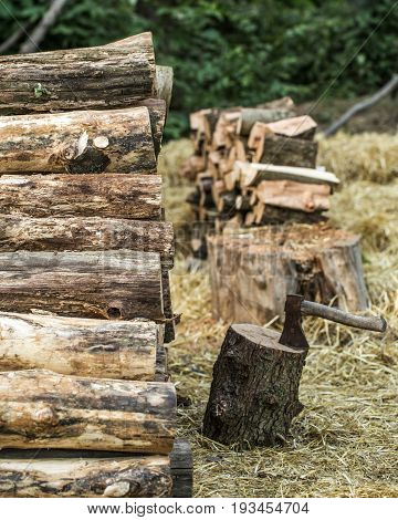 A deck of stacked logs and an axe in a log, the concept of drilling wood