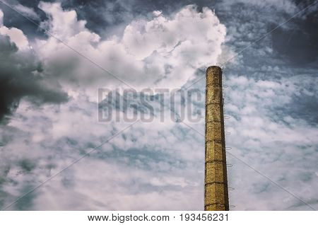 Old brick smoking chimney with dramatic sky background. Environmental protection concept.