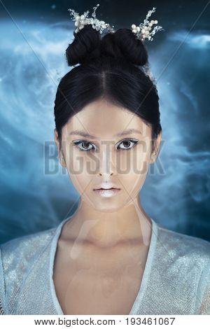 Portrait of futuristic young woman. Beautiful young multi-racial Asian Caucasian model girl in silver urban clothes with conceptual hairstyle and make-up against space background looking at camera. Sci-fi poster style.