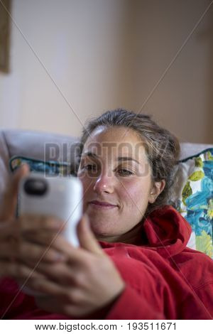 Young caucasian woman lying on a couch looking at her smartphone.