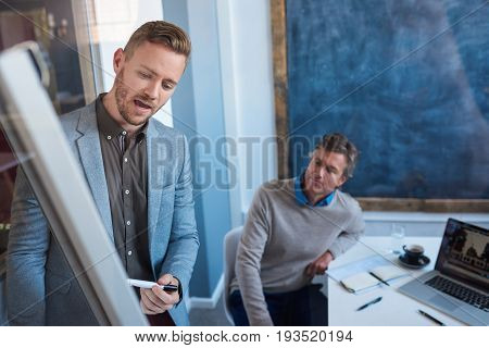 Young businessman explaining his ideas on a whiteboard during a presentation to colleagues in the meeting room of a modern office