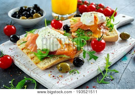 Poached egg on grilled toast with smoked salmon, rucola, olives, vegetables and orange juice. on white board. healthy breakfast.