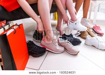 Close-up photo of female legs choosing sports footwear trying on different sneakers in a shopping mall.
