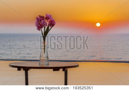 Vase of flowers on table by the swimming pool overlooking sea at sunset in Pomos village Paphos area Cyprus
