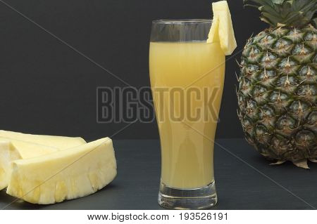A glass with pineapple juice, a whole pineapple and pineapple chunks