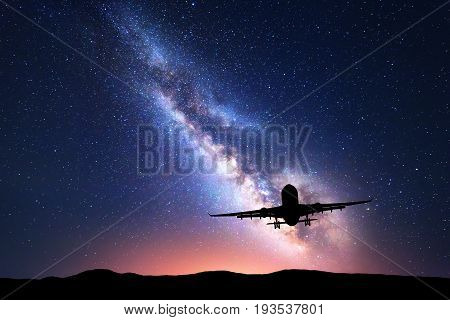 Milky Way and silhouette of a airplane. Landscape with passenger airplane is flying in the starry sky at night. Space background. Commercial airliner on the background of colorful Milky Way. Aircraft