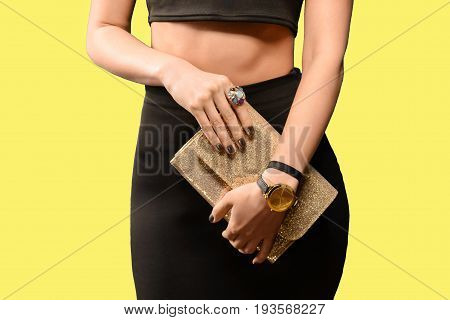 Trendy young girl in black skirt holding golden leather handbag yellow background