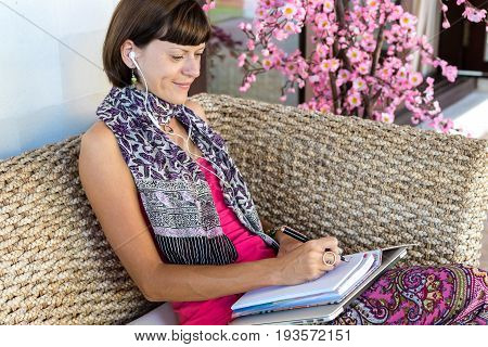 Beautiful young woman with notebook and laptop in the wooden coach outdoors on villa.