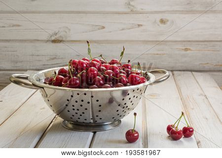 Metal strainer or bowl with ripe berries and cherry on wooden background. Colander filled with fresh cherries over a rustic board.