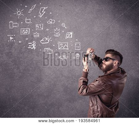 An elegant hipster guy trying to use a vintage camera with camera settings icons drawn on wall, like flash, white balace or ISO value concept