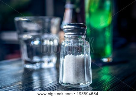 Close up image of bottle salt shaker on a wooden table in cafe.