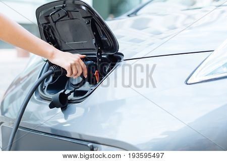 Environment conscious. Beautiful dainty female hands holding an electrical nozzle and charging a state-of-the-art electric car