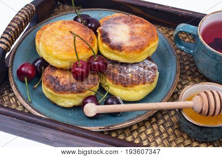 Delicious curd cheese cakes with honey and cherries on tray. Studio Photo