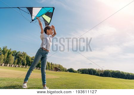 side view of little girl wanting to launch a kite on green lawn