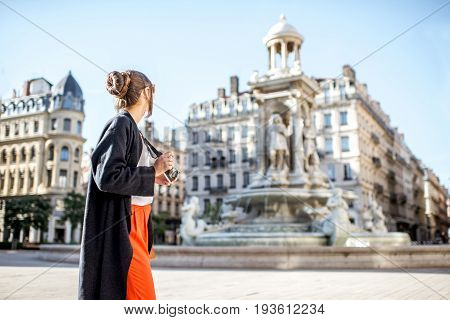 Young woman standing with photo camera on the Jacobins square with famous fountain on the background in Lyon city in France