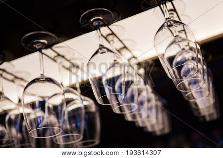 Empty wine glasses hanging upsidedown in bar interior. Classic wineglasses hanger on restaurant or pub background