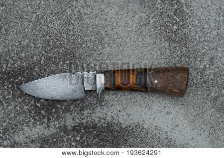 A hand forged Damascus hunter knife displayed on cement