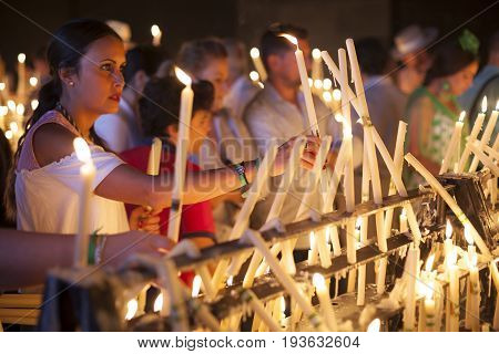 El Rocio Spain - June 2 2017: Female pilgrim in traditional spanish dress lights up candles in the hermitage of El Rocio during the Romeria 2017. Andalusia Spain