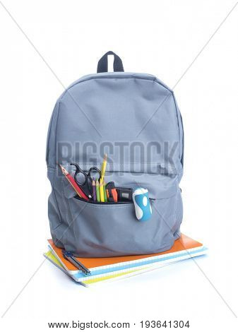 Backpack with school supplies on top of notebooks, isolated on white