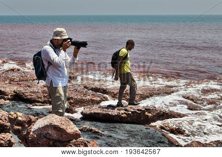 Hormuz Island Hormozgan Province Iran - 17 april 2017: Two tourists walk along the beach of the volcanic island and take photographs.