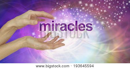 Miracles Happen background - female cupped hands with the word MIRACLES floating between  on a swirling multi-coloured background with glittering sparkles and copy space