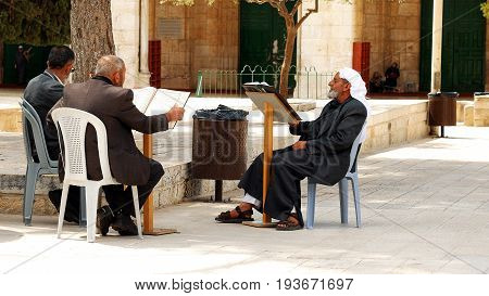 Jerusalem, Israel - May 21, 2017: Three senior Muslims pray and read the Quran at the entrance of Al-Aqsa mosque in Jerusalem or Quddus. Al Aqsa mosque is a sacred place for all muslims and islamic