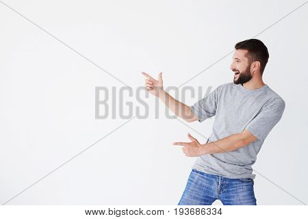 Cheerful male pointing with both hands on white field aside, bending back a bit, wearing grey T-shirt, mid shot