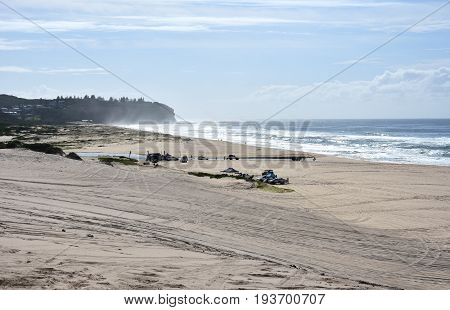 Horizontal landscape of the beach with cars. 4wd cars at Crokers creek (Belmont - Nine Miles - Beach NSW Australia). Redhead Point in the background.