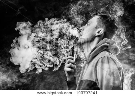 Vape. Young handsome white guy is admiting puffs of steam from the electronic cigarette.Black and white photo.