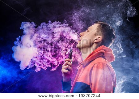 vaping man holding a mod. A cloud of vapor. dark blue background.